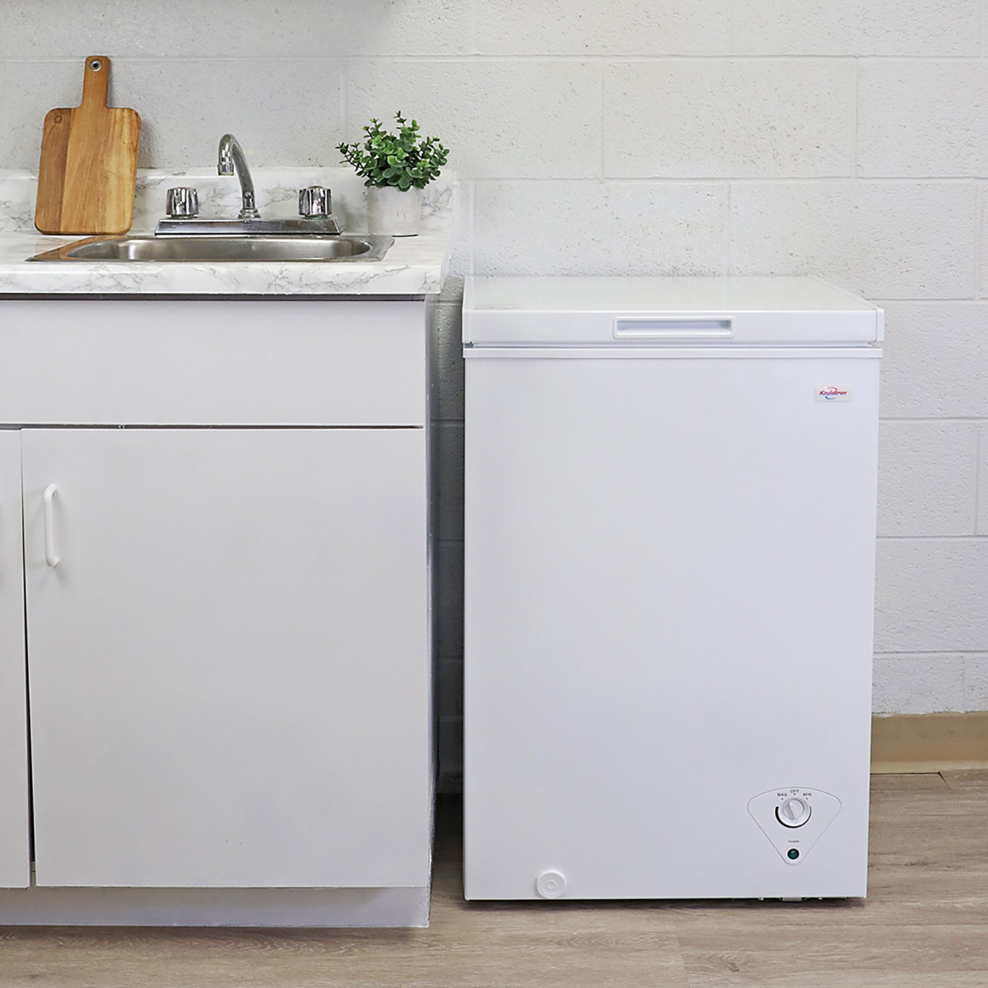 Koolatron white chest freezer, closed, beside a white kitchen cabinet with white marble countertop
