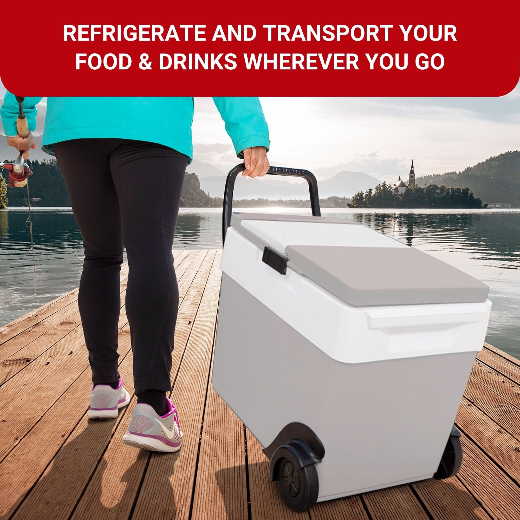 A person wearing black pants, running shoes, and an aqua jacket holding a fishing pole in one hand and towing the Kool-atronrolling 12V cooler/warmer with the other on a wooden dock extending into a calm lake with a tree-covered shoreline in the distance.Text above reads, "REFRIGERATE AND TRANSPORT YOUR FOOD AND DRINKS WHEREVER YOU GO"