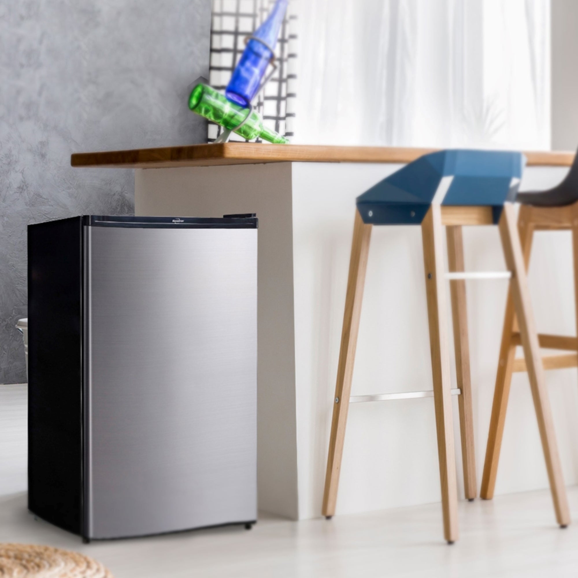 Black and stainless steel compact fridge with freezer beside a white breakfast bar with wooden countertop and two wood and plastic bar stools