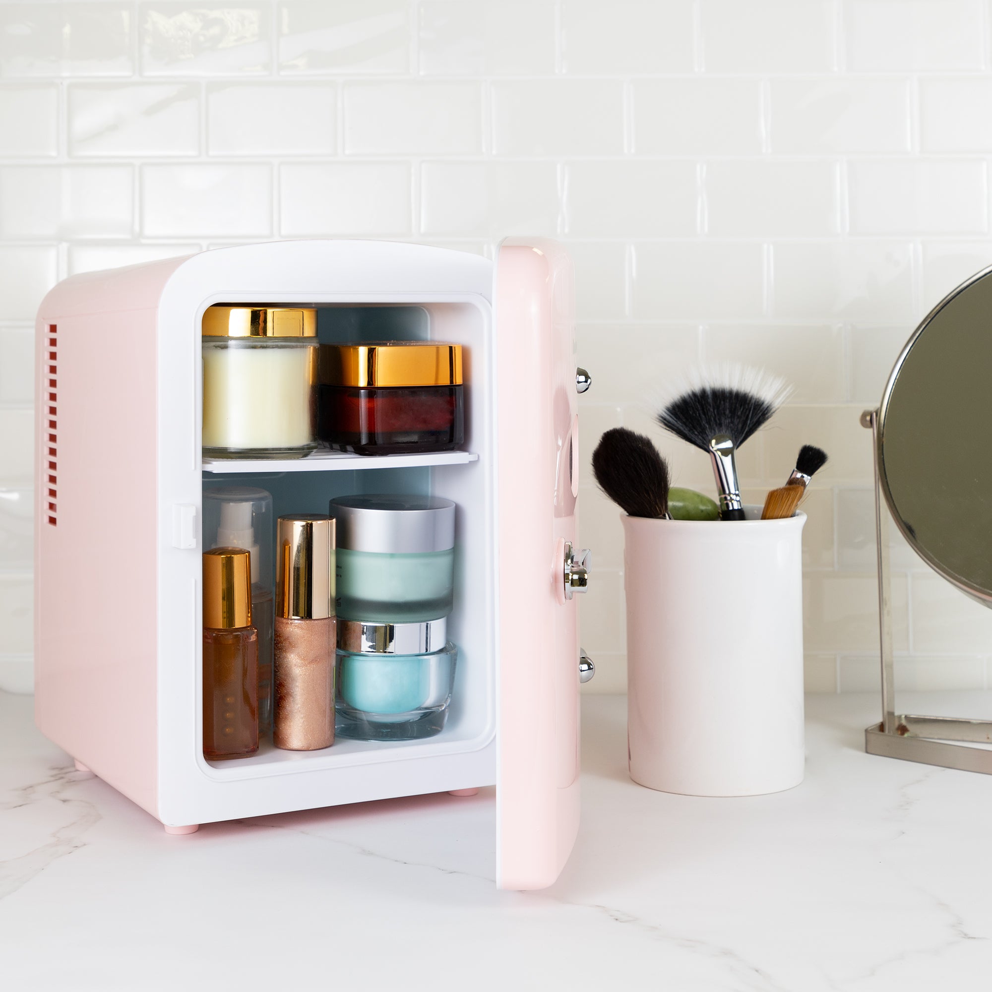 Lifestyle image of Kool-atronretro 6 can mini fridge, open with cosmetics and skincare products inside, with makeup brushes in a white container on its right, on a white marbled counter with a white tile backsplash behind